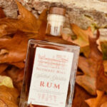 Netherby Hall Walled Garden Rum bottle placed among autumn leaves, featuring a square shape, wooden cork stopper, and elegant label inspired by the historic gardens.