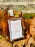 Netherby Hall Walled Garden Rum bottle nestled in a bed of autumn leaves, featuring a rectangular design with a wooden cork and elegant label.