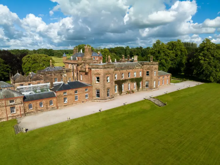 Breathtaking aerial view of Netherby Hall surrounded by lush green lawns and scenic countryside.