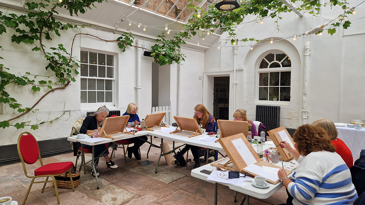 Participants working on botanical illustrations in the Orangery at Netherby Hall, surrounded by vine-covered walls and natural light