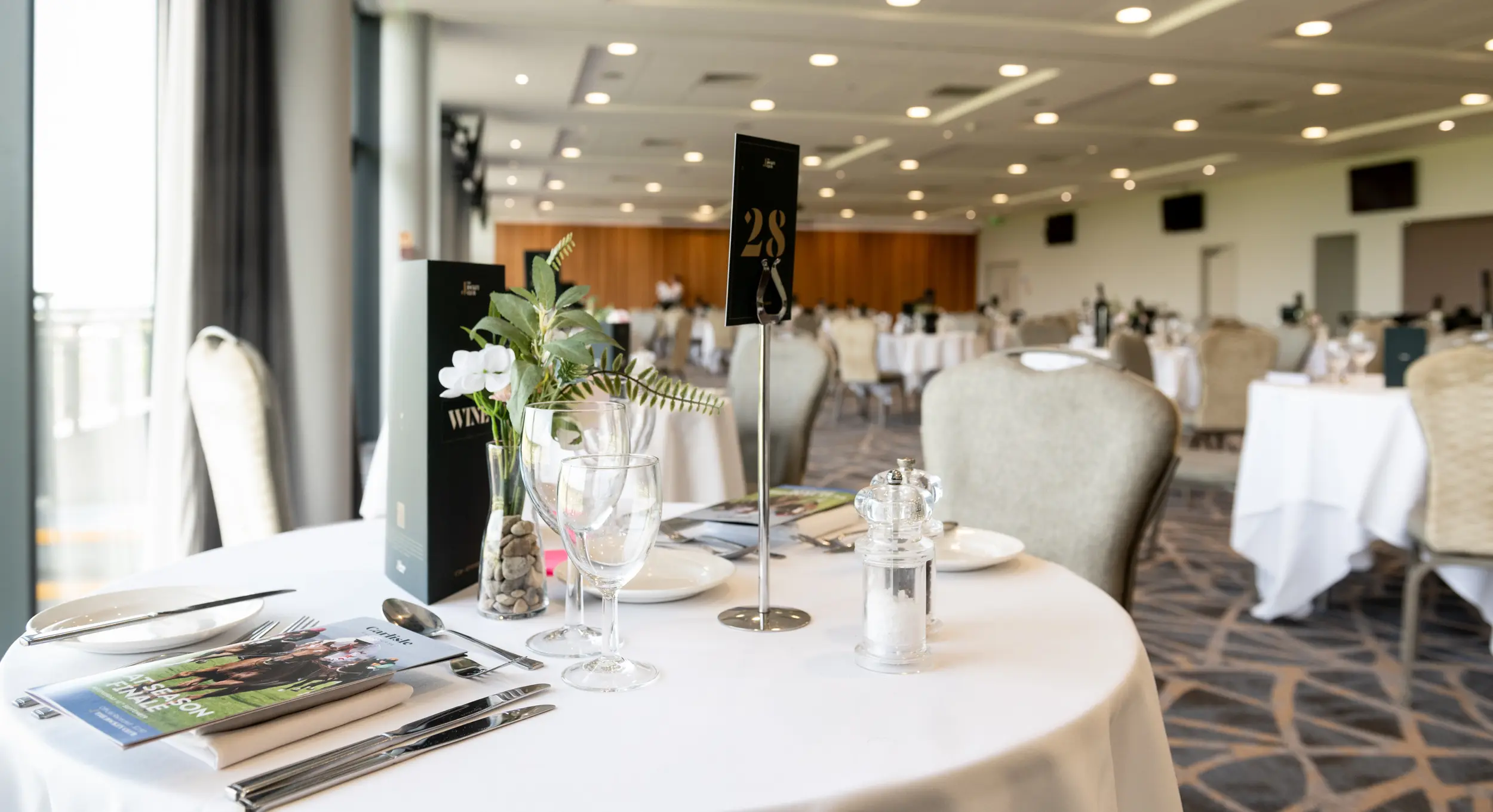 Elegant dining setup featuring a beautifully arranged table with glassware, cutlery, and floral decor in a spacious restaurant setting at Netherby Hall, showcasing luxury self-catering accommodation in Cumbria.