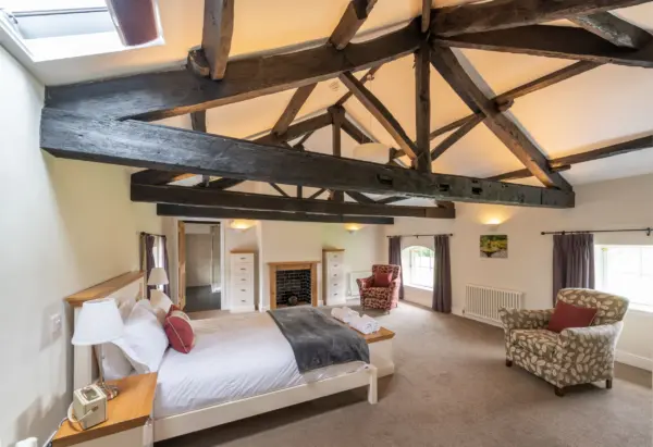 Luxury self-catering accommodation at Netherby Hall in Cumbria featuring a spacious bedroom with exposed wooden beams, elegant furnishings, and cozy seating areas, ideal for a relaxing getaway.