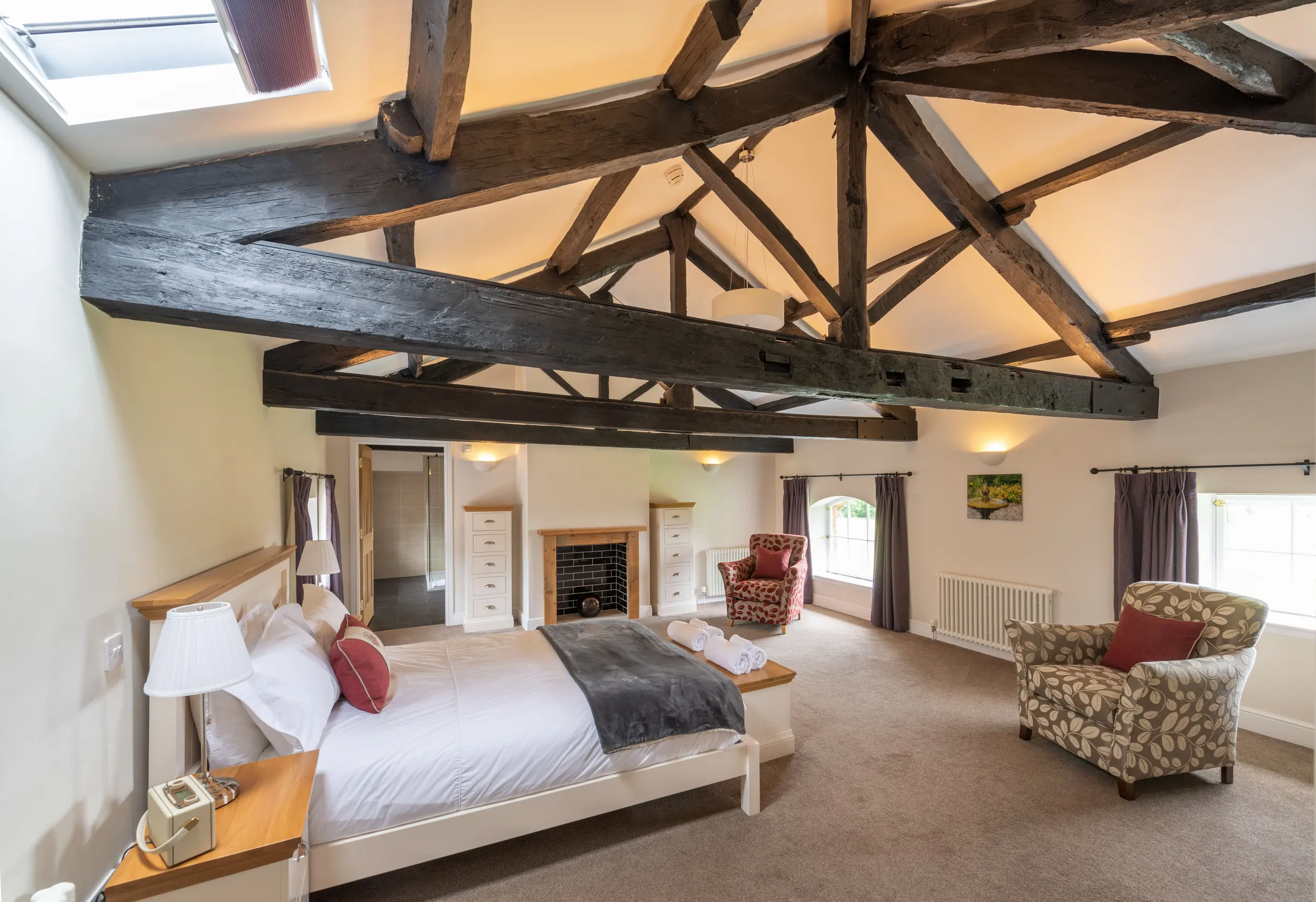Luxury self-catering accommodation at Netherby Hall in Cumbria featuring a spacious bedroom with exposed wooden beams, elegant furnishings, and cozy seating areas, ideal for a relaxing getaway.