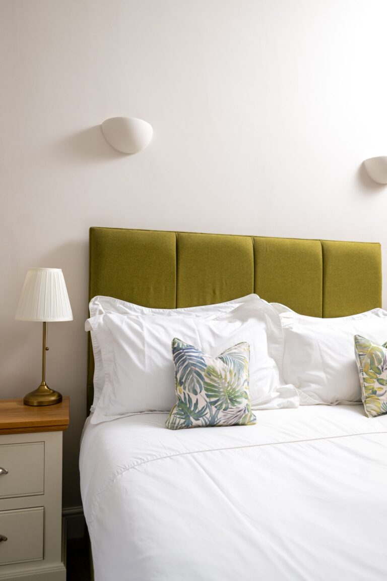 Luxury double bed with a chartreuse green velvet headboard and white linens in the Clock Tower Apartment at Netherby Hall, Cu