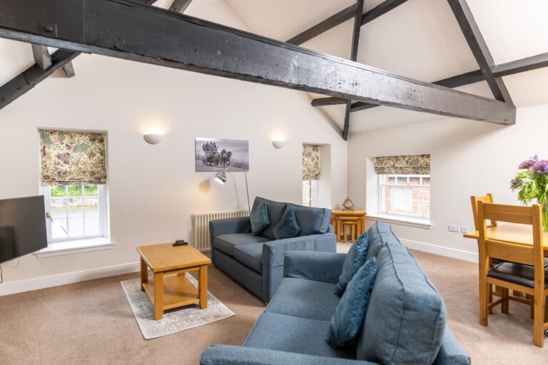 Living room of the Clock Tower Apartment at Netherby Hall, featuring blue sofas and exposed wooden beams in a luxury self-catering Cumbria rental