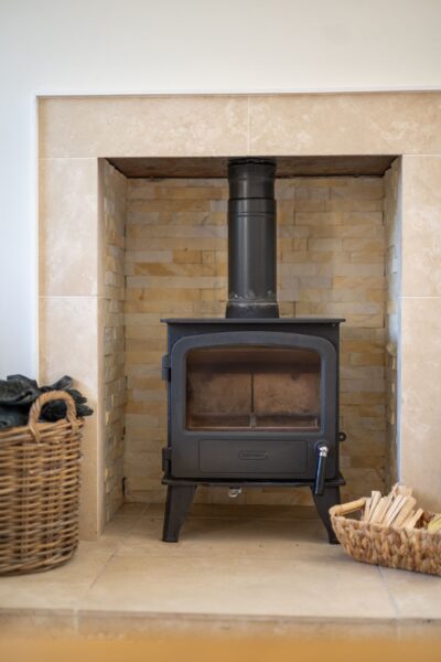 Black wood-burning stove in a stone fireplace at the Coach House luxury self-catering apartment, Netherby Hall, Cumbria