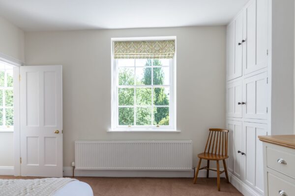 Bright bedroom in the Coach House apartment featuring a large window with garden views, a white radiator, and tall built-in wardrobes