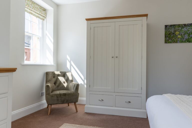 Armchair and white wardrobe in a bright bedroom at the Coach House self-catering apartment at Netherby Hall, Cumbria