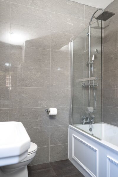Modern bathroom in the Coach House apartment featuring a white bathtub with a glass shower screen and grey tiled walls