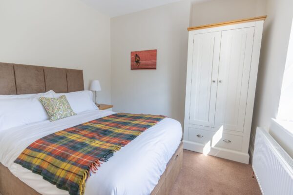 Bedroom at the Coach House apartment featuring a large bed with a plaid throw and a white wardrobe in a luxury self-catering Cumbria accommodation