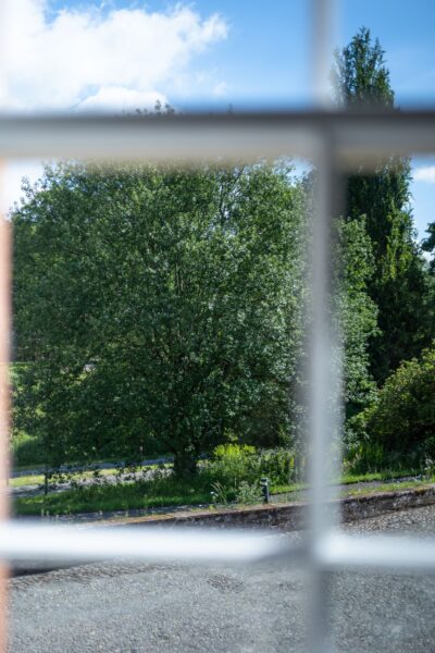 View of lush green trees and gardens through a window at the Coach House luxury self-catering accommodation in Cumbria