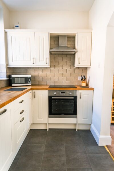 Modern kitchen with white cabinetry, wooden countertops, and stainless steel appliances in the Coach House luxury apartment at Netherby Hall