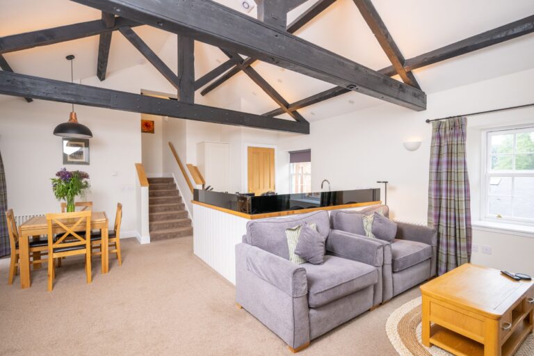 Modern living area in Engineer Apartment at Netherby Hall featuring exposed wooden beams, grey armchairs, and a wooden dining set