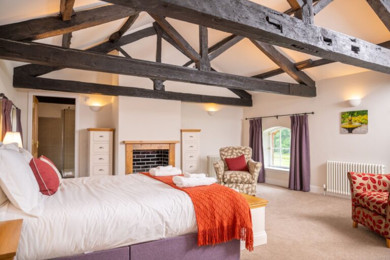 Brightly lit bedroom in the Engineer Apartment at Netherby Hall featuring rustic exposed wooden beams and a large bed with orange accents