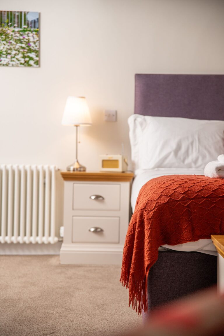 Bedroom in the Engineer Apartment at Netherby Hall featuring a cozy bed with a red throw, bedside table, and lamp
