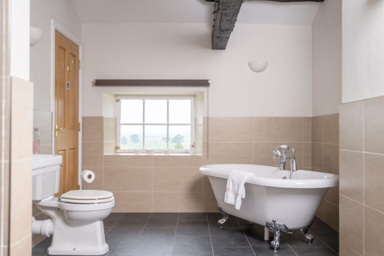 White clawfoot bathtub and toilet in a modern luxury bathroom at the Engineer Apartment, Netherby Hall