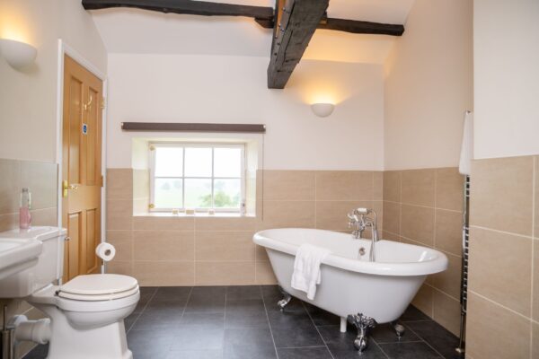 Modern bathroom in Engineer Apartment featuring a white clawfoot bathtub, beige tiles, and exposed wooden ceiling beams