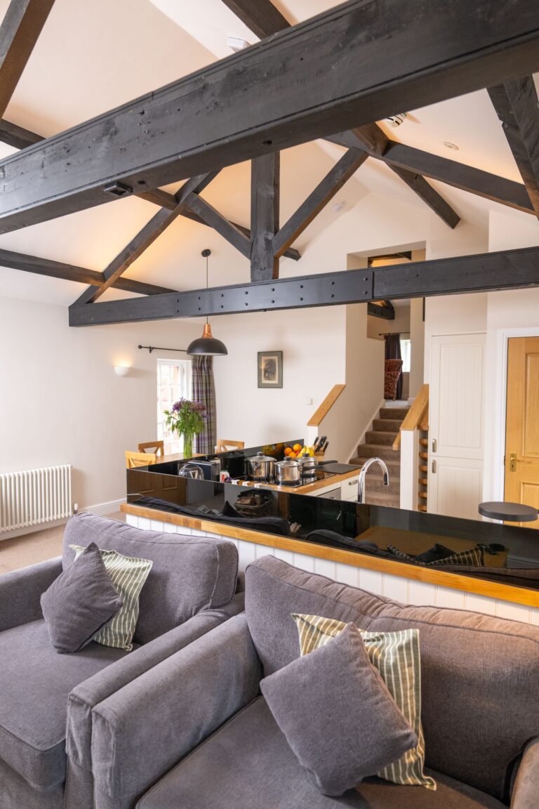 Modern living room and kitchen area in the Engineer Apartment at Netherby Hall featuring dark wooden ceiling beams and grey sofas