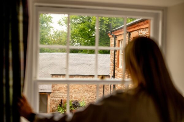 Woman looking out a window at the stone courtyard of the Engineer Apartment at Netherby Hall, luxury self-catering accommodation in Cumbria