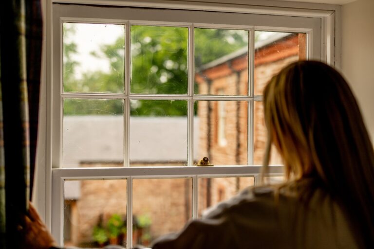 A woman looking out of a large window at the Engineer Apartment in Netherby Hall, Cumbria