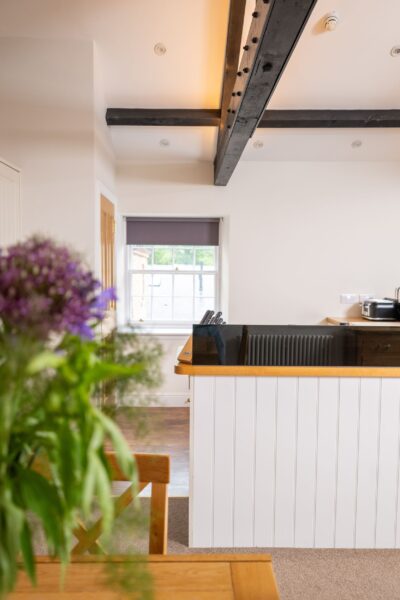Modern kitchen interior featuring a white breakfast bar and dark wooden ceiling beams in the Engineer Apartment at Netherby Hall