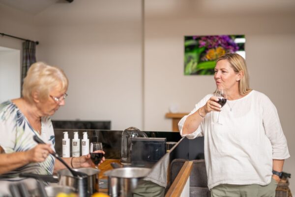 Two women enjoying red wine and cooking together in the modern kitchen of the Engineer Apartment at Netherby Hall, Cumbria