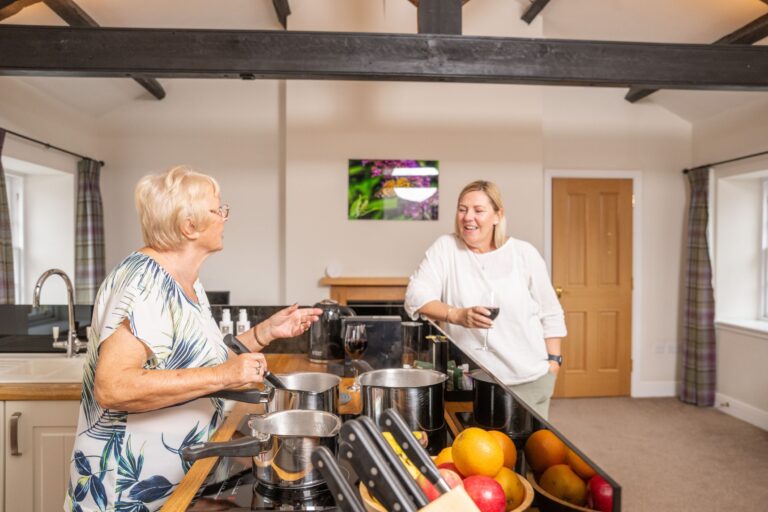 Two women laughing and cooking together in the modern kitchen of the Engineer Apartment at Netherby Hall