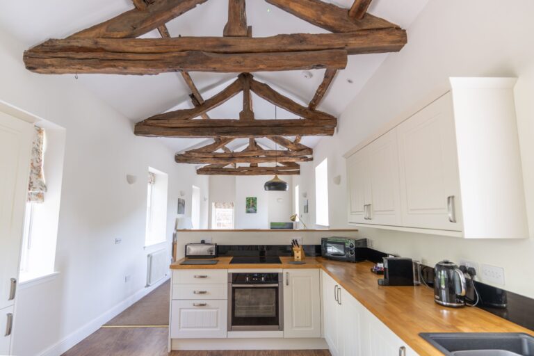 Modern kitchen in the luxury Gardener's Cottage at Netherby Hall, featuring rustic wooden ceiling beams and white cabinetry