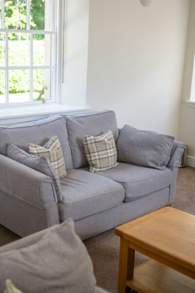 Grey sofa with plaid cushions next to a window in the luxury Gardener's Cottage at Netherby Hall, Cumbria