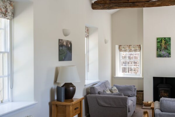 Living room in Gardener's Cottage at Netherby Hall, featuring a grey sofa, wooden accents, and large windows in a luxury Cumbria apartment