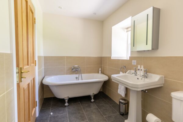 Modern bathroom in Gardener's Cottage featuring a classic white clawfoot bathtub and pedestal sink at Netherby Hall, Cumbria