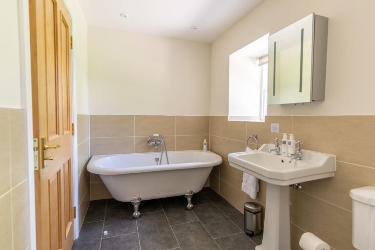 Modern bathroom in Gardener's Cottage featuring a classic white clawfoot bathtub and pedestal sink at Netherby Hall, Cumbria
