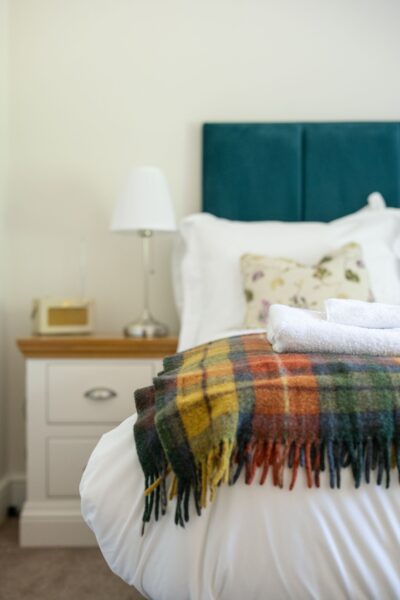 Bedroom interior of Gardener's Cottage featuring a bed with a plaid throw, white linens, and a teal headboard at Netherby Hall