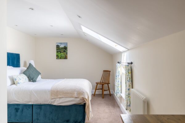 Bright bedroom in Gardener's Cottage featuring a large bed with blue velvet headboard and a skylight window