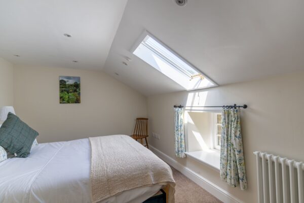Bright bedroom in Gardener's Cottage with a skylight, white linens, and floral curtains at Netherby Hall, Cumbria