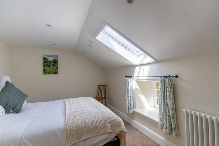 Bright bedroom in Gardener's Cottage with a skylight, white linens, and floral curtains at Netherby Hall, Cumbria