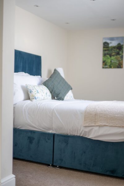 Bedroom with a blue velvet headboard and white linens in the Gardener's Cottage at Netherby Hall, Cumbria