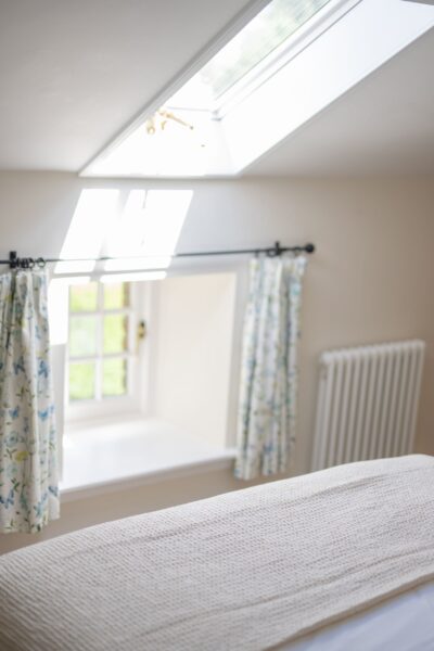 Bright bedroom in Gardener's Cottage featuring a skylight, window seat, and floral curtains at Netherby Hall, Cumbria