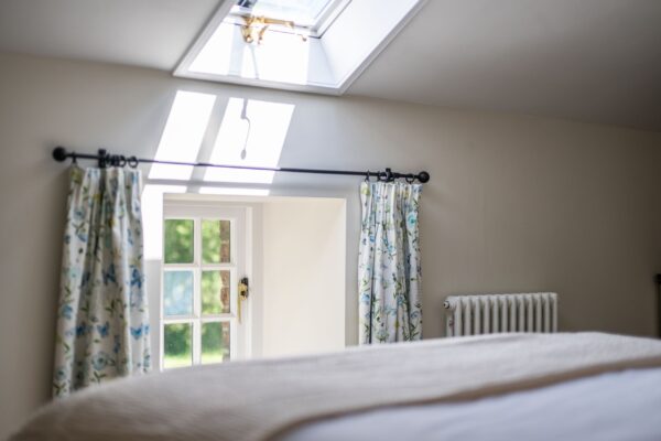 Bright bedroom interior at Gardener's Cottage featuring a skylight, floral curtains, and a window overlooking the Netherby Hall grounds