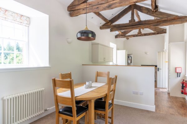 Dining area in Gardener's Cottage featuring a wooden table, chairs, and rustic exposed timber beams at Netherby Hall