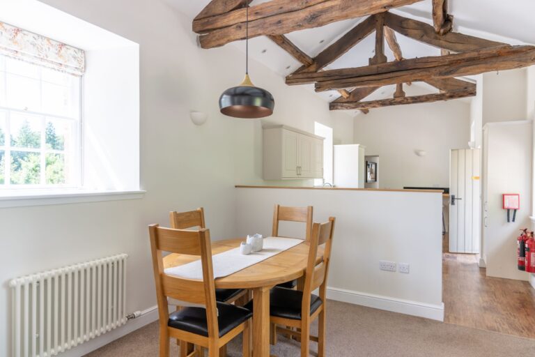 Dining area in Gardener's Cottage featuring a wooden table, chairs, and rustic exposed timber beams at Netherby Hall