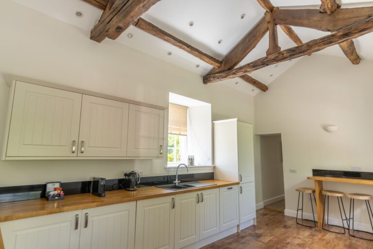 Modern kitchen in the Gardener's Cottage at Netherby Hall, featuring rustic wooden ceiling beams and white cabinetry
