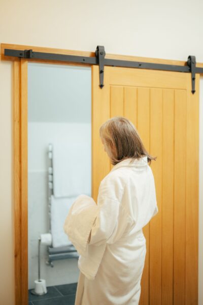 A woman in a white bathrobe looking into a mirror inside the luxury Grooms' Quarters apartment at Netherby Hall