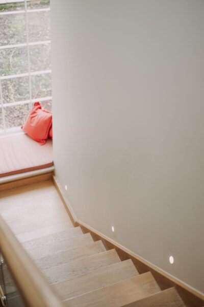 Wooden staircase with built-in lighting and a window seat with red cushions in the Grooms' Quarters luxury self-catering apartment