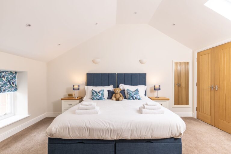 Bright and airy bedroom with a large blue headboard and white linens in the Grooms' Quarters luxury self-catering apartment at Netherby Hall