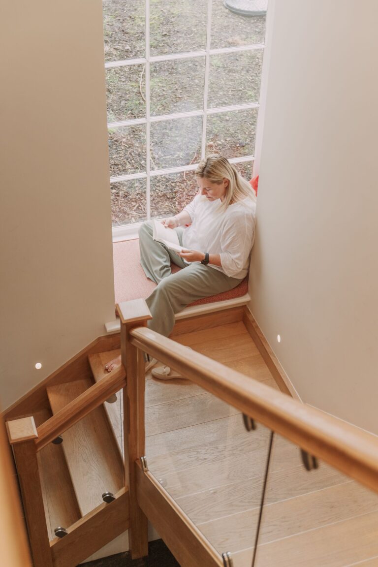 Woman reading a book while sitting by a large window in the Grooms' Quarters luxury self-catering apartment at Netherby Hall, Cumbria