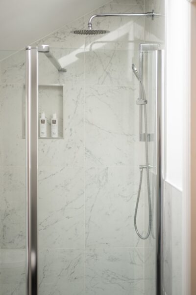 Modern walk-in shower with marble tiling and chrome fixtures in the Grooms' Quarters luxury self-catering apartment at Netherby Hall