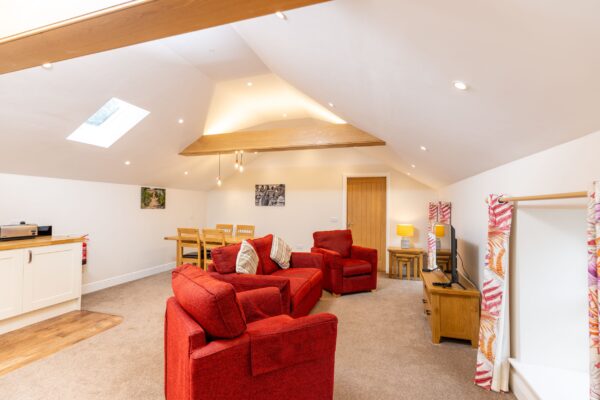Bright and spacious living area in the Grooms' Quarters apartment at Netherby Hall, featuring red sofas and a dining area under sloped ceilings