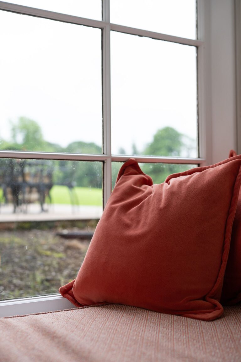 Terracotta colored pillow resting on a cushioned window seat at Grooms' Quarters luxury self-catering apartment in Cumbria