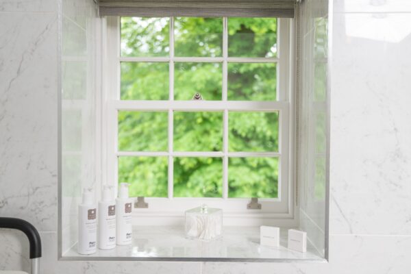 Window view of lush greenery from an Independent Apartment at Netherby Hall, featuring luxury toiletries on a marble sill
